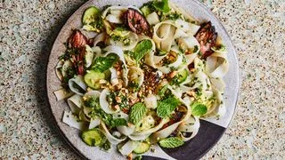 A plate of wide flat rice noodles tangled with sliced steak, cucumbers, mint leaves, and peanuts.